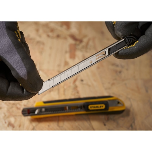 Photo of STANLEY 0-11-300 snap-off utility knife blade being replaced, with gloved hands, on wood surface.