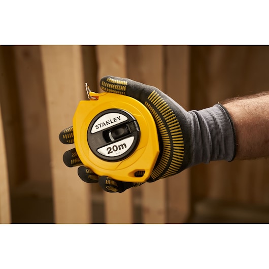 Stanley 0-34-107 yellow 20m tape measure held in gloved hand, photography construction setting.