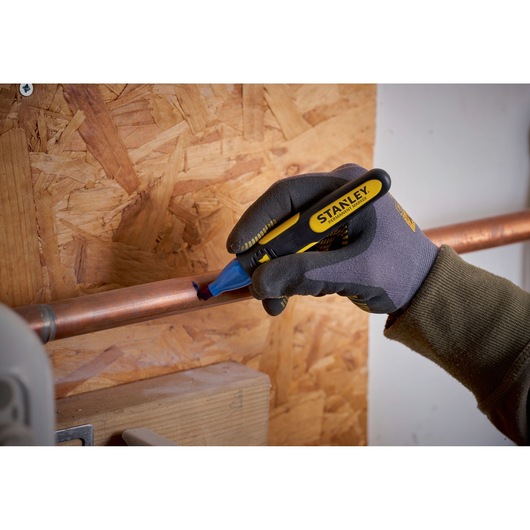 Stanley 0-47-315 pipe marker held by gloved hand marking copper pipe near wooden wall.