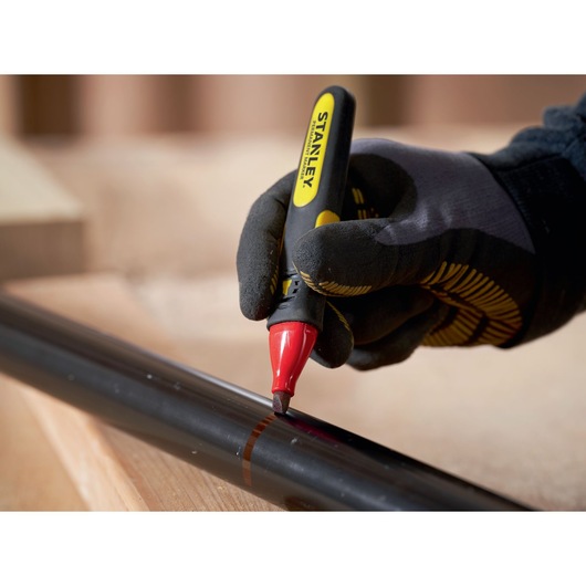 Photo of STANLEY 0-47-315 marker pen with red tip marking a black pipe, worn by gloved hand.