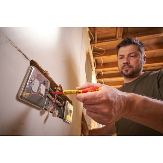 Photo of STANLEY 0-65-410 insulated screwdriver used for electrical socket wiring by a person.