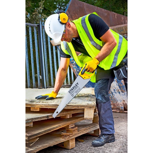 STANLEY 1-20-087 hand saw with yellow and black handle used to cut wood boards, shown in a construction setting.