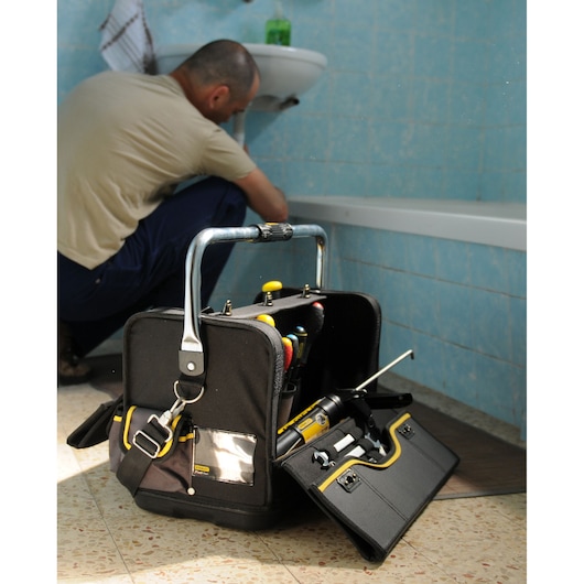 Photo of STANLEY 1-70-719 tool bag filled with tools, placed on bathroom floor, plumber working by sink.