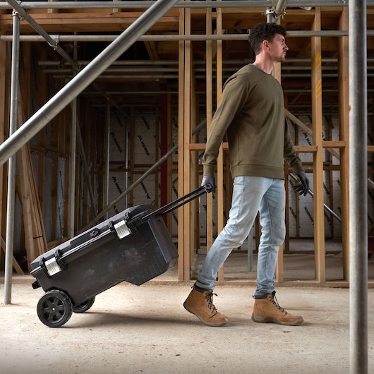 STANLEY 1-94-850 mobile tool box with handle being pulled by a person at a construction site.