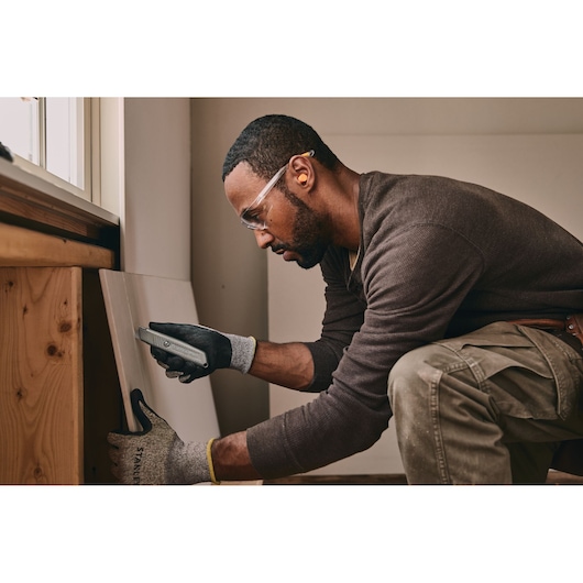 Photo of STANLEY 10-299 utility knife cutting drywall held by gloved hand during construction work.