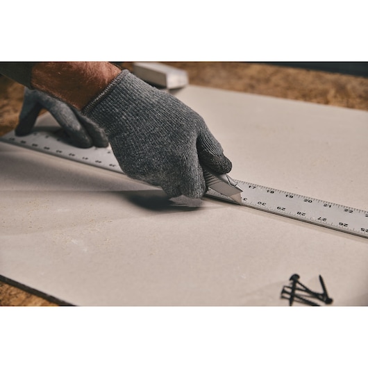 Stanley 10-299 utility knife cutting drywall alongside metal ruler, photography close-up of hand in glove.