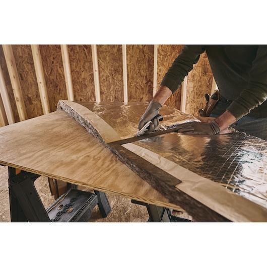 STANLEY 10-788 utility knife cutting reflective insulation on plywood in a workshop, side angle.