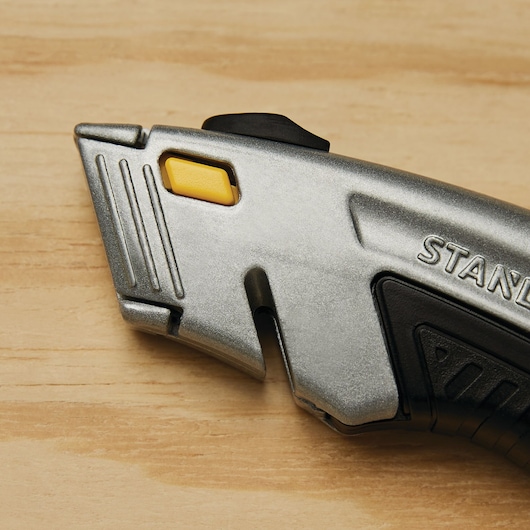 STANLEY 10-788 utility knife close-up, silver metal body with yellow button, angled on wood surface.