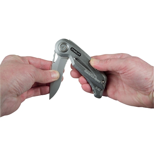 Photo of STANLEY 10-813 folding utility knife being opened by hand, showing metallic handle and partially serrated blade.