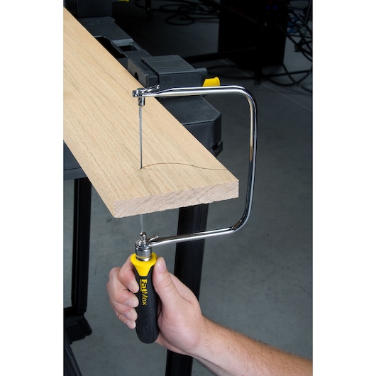 STANLEY 15-104 coping saw with yellow and black handle cutting curved line in wood, close-up side view.