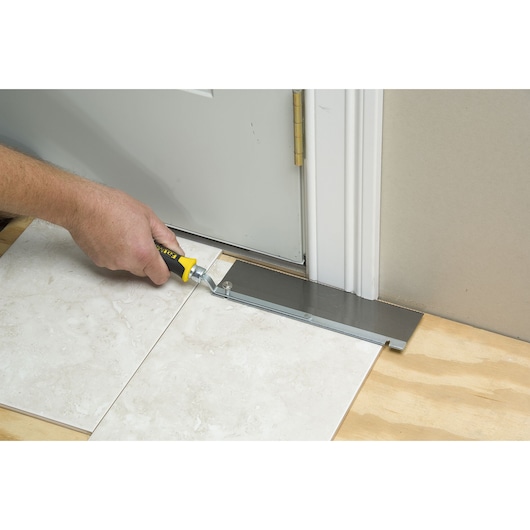 STANLEY 15-252K hand saw cutting door jamb near floor tiles, side angle.