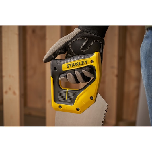 Photo of STANLEY 2-15-599 hand saw with yellow and black handle, held by gloved hand, woodworking background.