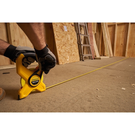 Photo of a STANLEY 34-791 open reel long tape measure being used on a construction floor.