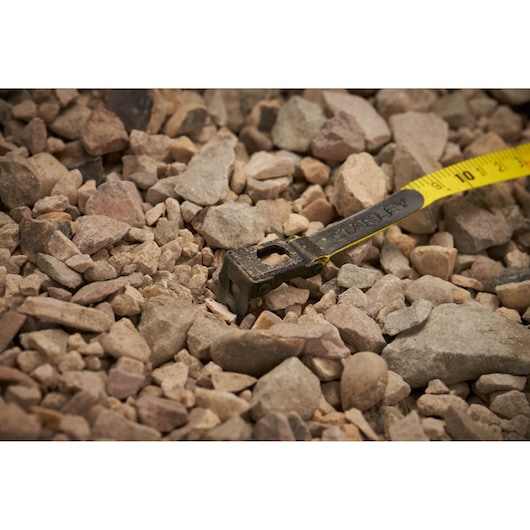 STANLEY 34-791 tape measure end on rocky ground, showing yellow blade, close-up angle.