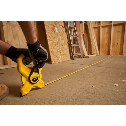 Photo of STANLEY 2-34-792 tape measure with 30m yellow blade in use on construction floor, gloved hand holding tool.