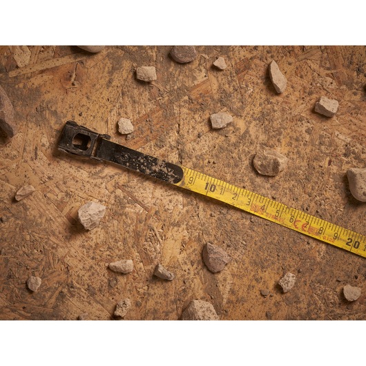 STANLEY 2-34-794 tape measure close-up on dusty plywood with scattered rocks, photography product.