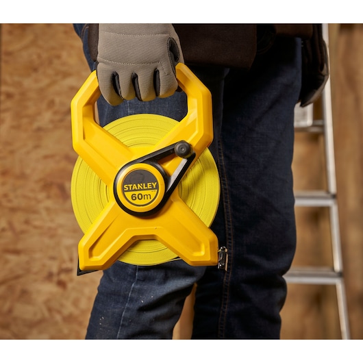 STANLEY 2-34-795 measuring tape 60m held by person wearing gloves, close-up, indoor work setting.