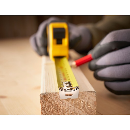 STANLEY 30-393 tape measure photography close-up on wood piece with gloved hand and pencil.