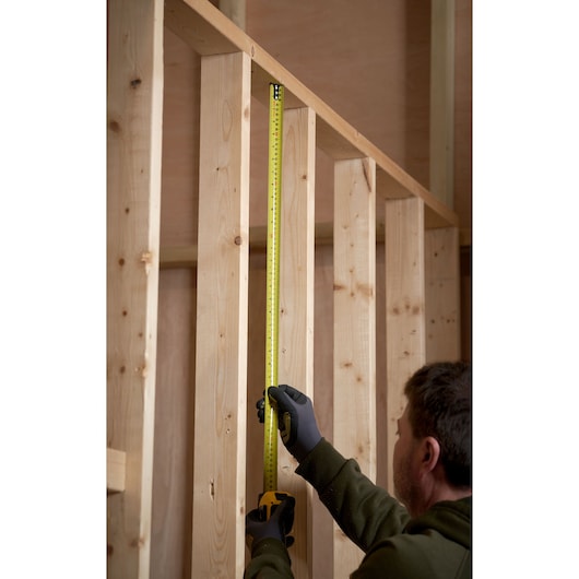 Photo of STANLEY 33-731 tape measure held vertically against wooden studs during construction.
