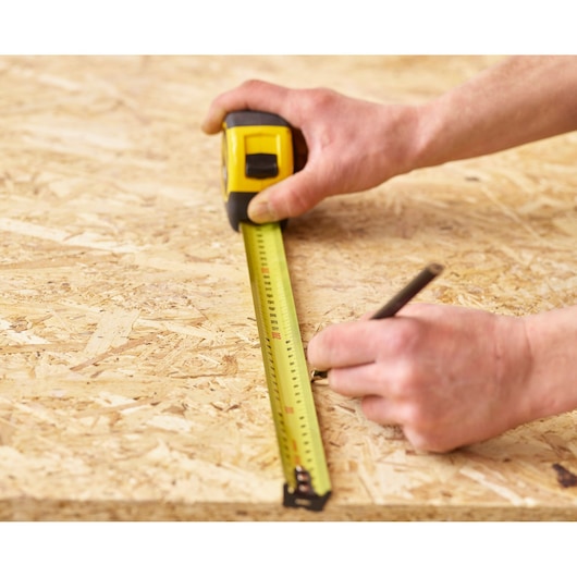 STANLEY 33-732 tape measure on wood surface, person marking with pencil, close-up photography.