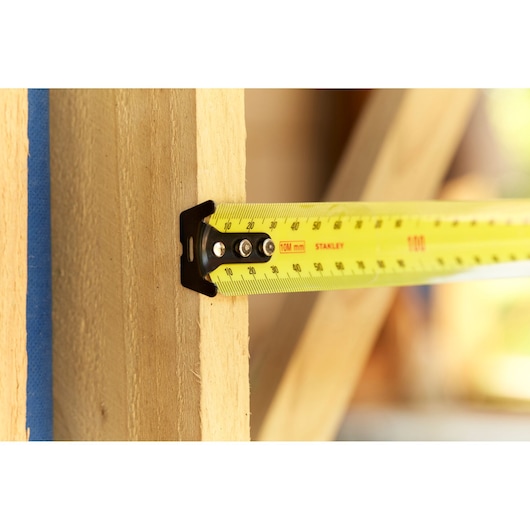 STANLEY 33-829 yellow tape measure in use measuring wooden beam, close-up photography.