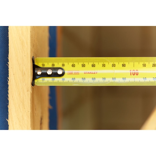 STANLEY 33-829 yellow tape measure in use measuring wooden plank, close-up side angle.