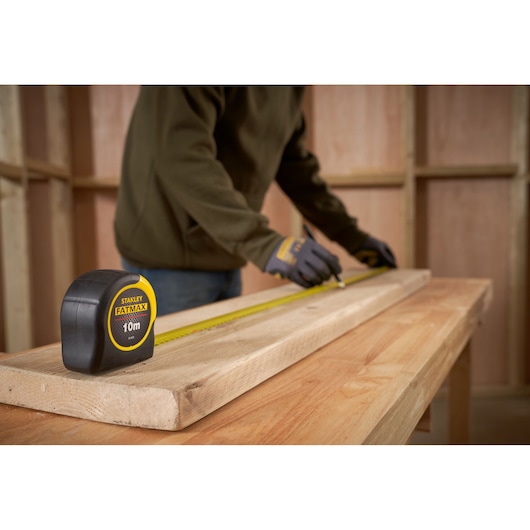 STANLEY 33-829 tape measure on wood, person marking lumber in workshop, product photography.