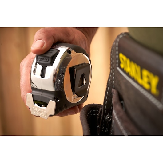 STANLEY 5-33-893 tape measure held in hand near tool belt, close-up photography.