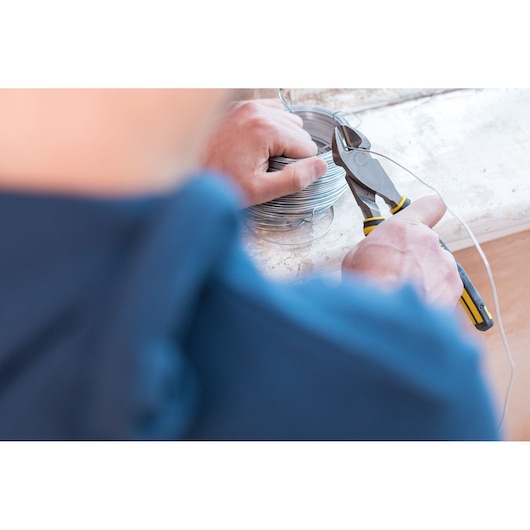 Photo of STANLEY 89-859 wire cutter pliers in use, cutting metal wire with yellow and black handle, close-up.