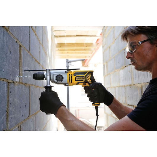 Stanley FME142K corded hammer drill in use on a brick wall, held by gloved hands.