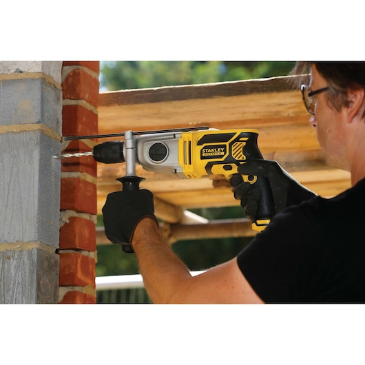 STANLEY FME142K hammer drill in use drilling into a brick wall, worker wearing gloves outdoors.