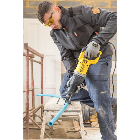 STANLEY FME360 reciprocating saw cutting blue pipe on workbench in workshop.