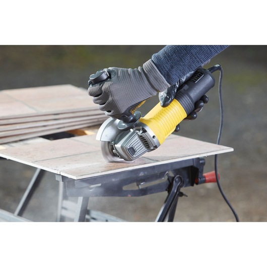 Photo of STANLEY FMEG220K angle grinder cutting ceramic tiles on a workbench.