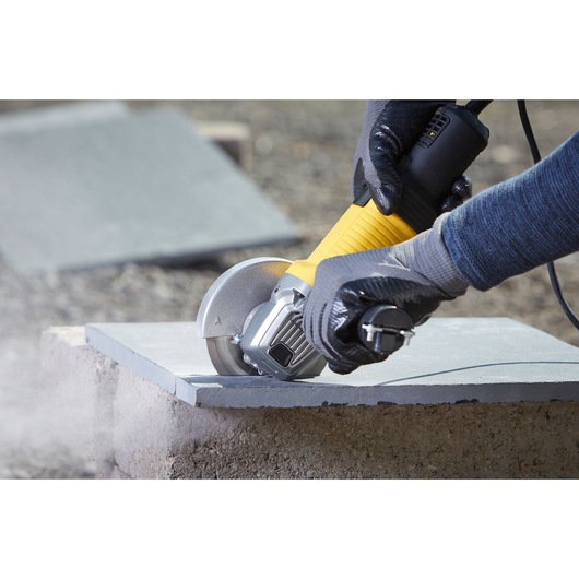 Photo of STANLEY FMEG220K angle grinder cutting stone, operator wearing gloves for safety.