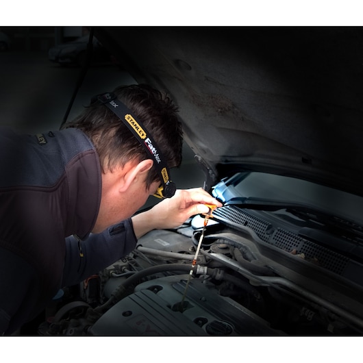 Photo of STANLEY FMHT0-70767 headlamp worn while inspecting car engine oil dipstick.