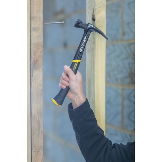 Stanley FMHT1-51277 claw hammer in use, black and yellow handle, construction scene.