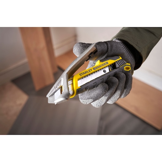 Photo of STANLEY FMHT10594-0 utility knife, yellow and black, held in gloved hand during cutting task.