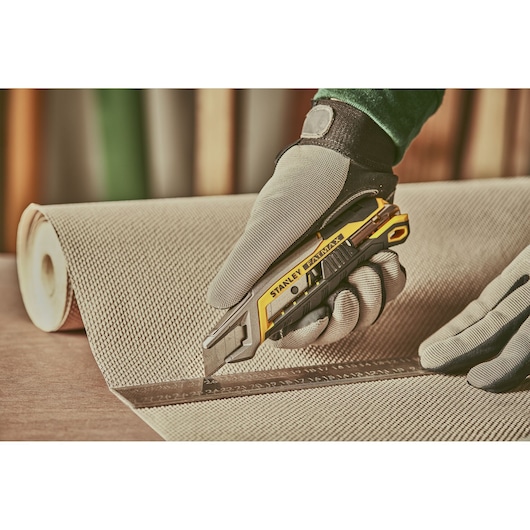 STANLEY FMHT10594-0 utility knife cutting fabric along a ruler, gloved hand visible, close-up photography.