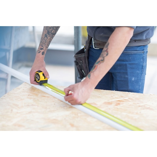 Photo of STANLEY FMHT36148-3 tape measure being used to measure a white strip on a wooden workbench.