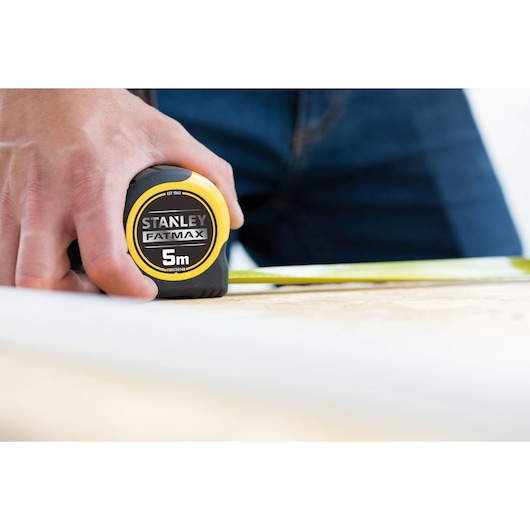 Photo of STANLEY FMHT36148-3 FATMAX 5m tape measure held by hand on wood surface.