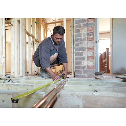 STANLEY FMHT36328 tape measure used by worker measuring pipes in house under construction.