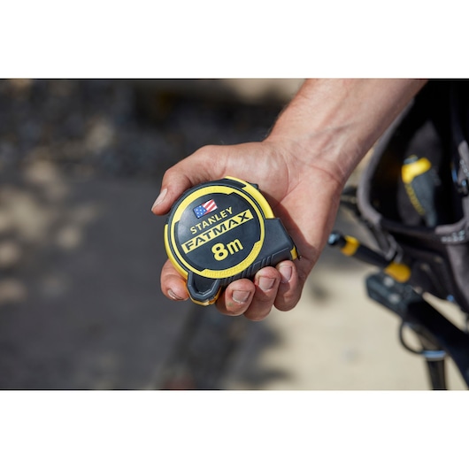 Photo of STANLEY FMHT36328 tape measure, FATMAX 8m, black and yellow casing, held in hand outdoors.
