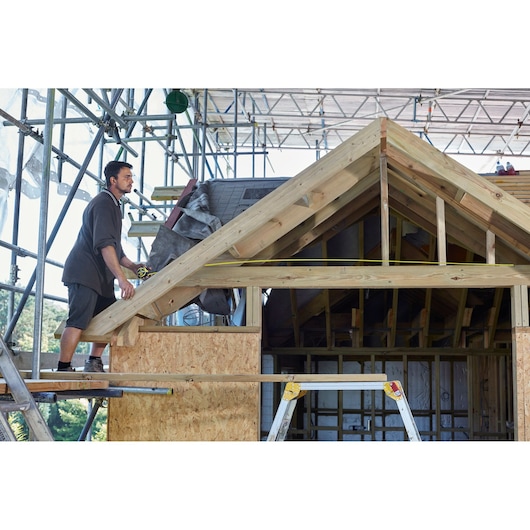 STANLEY FMHT36328 tape measure used on wooden roof frame at construction site.