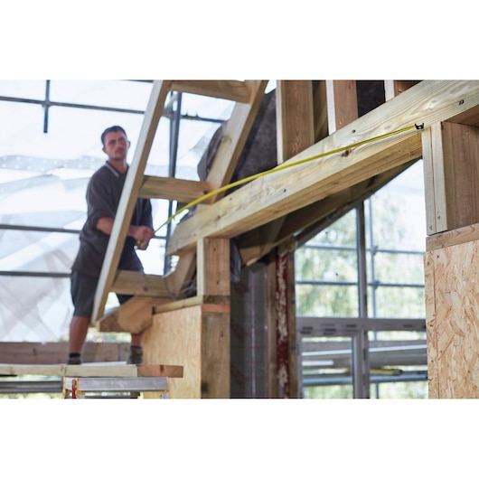 STANLEY FMHT36328 tape measure in use for measuring wooden beams during construction work.