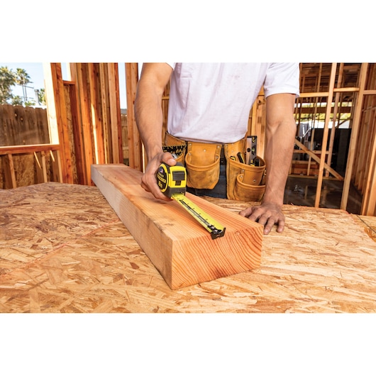 STANLEY FMHT36328 tape measure used by a worker to measure a wood beam on a construction site.