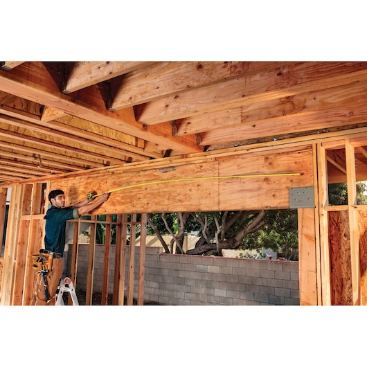 STANLEY FMHT36328 tape measure used by worker measuring wooden beam at construction site.