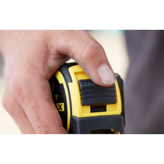 Close-up photo of hand using STANLEY FMHT36328 tape measure slider, black and yellow housing.