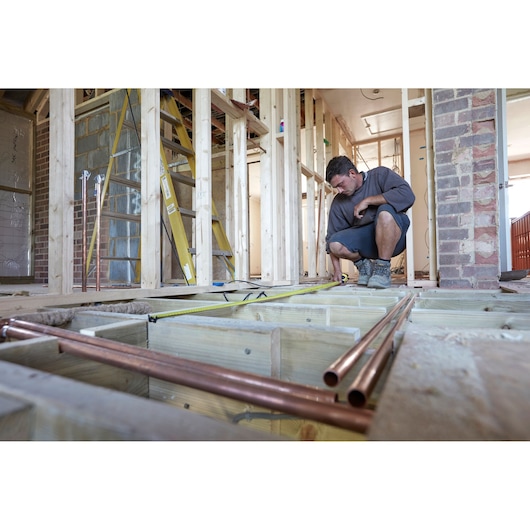STANLEY FMHT36328 tape measure used by worker in home construction, tape extended across wooden floor framing.