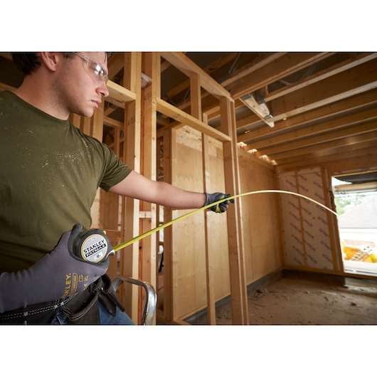 Photo of STANLEY FMHT38219-3 tape measure being used by a person wearing gloves at a construction site.