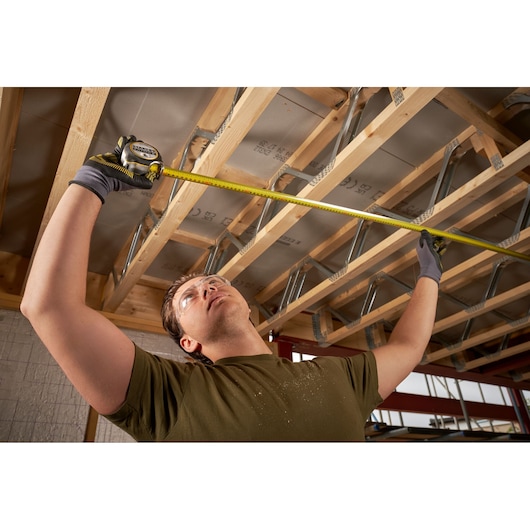 STANLEY FMHT38219-3 tape measure used by a person measuring ceiling joists, photography of product in use.